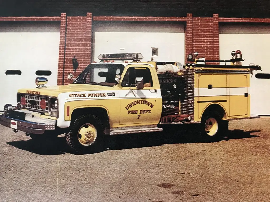 A vintage yellow and white Uniontown Fire Department attack pumper truck parked in front of a building with multiple garage doors.